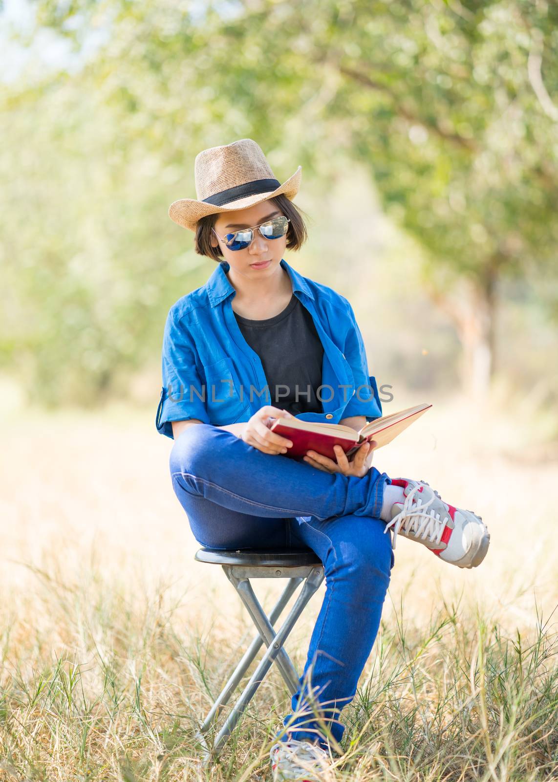 Young asian women short hair wear hat and sunglasses read a book ,sit on chair in countryside Thailand
