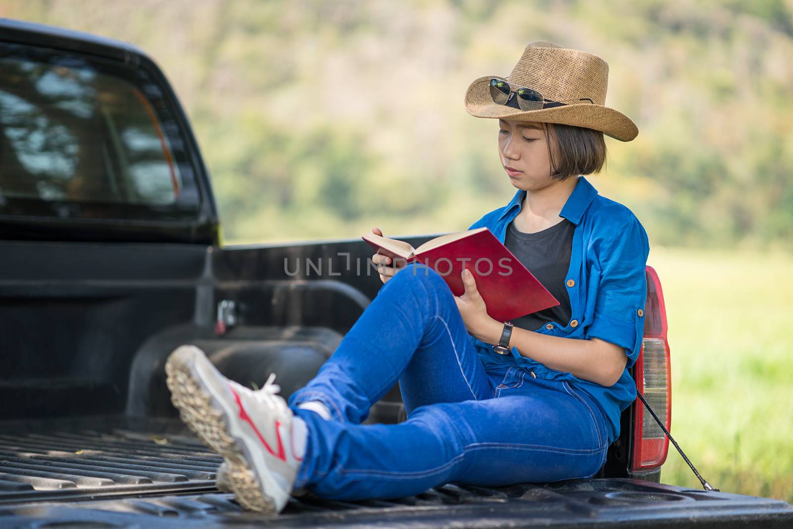 Woman wear hat and reading the book on pickup truck by stoonn