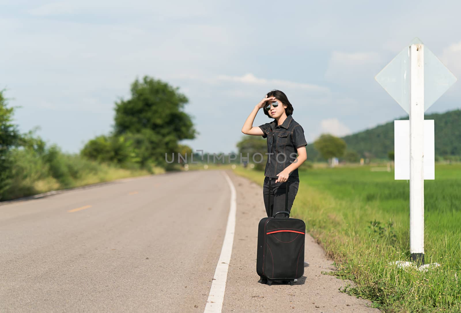 Woman with luggage hitchhiking along a road by stoonn