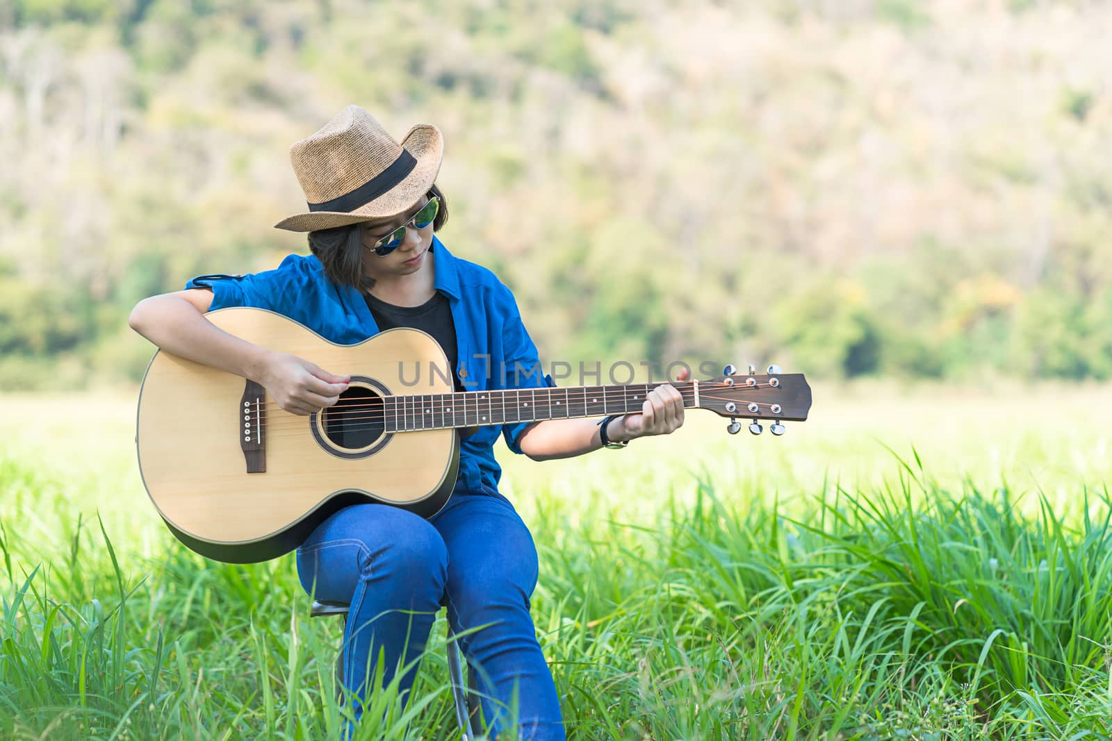Young asian women short hair wear hat and sunglasses sit playing guitar in grass field countryside Thailand