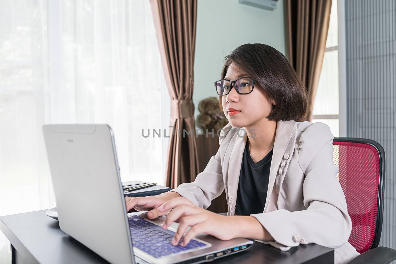 Young asian woman short hair in smart casual wear working on laptop while sitting near window in home office