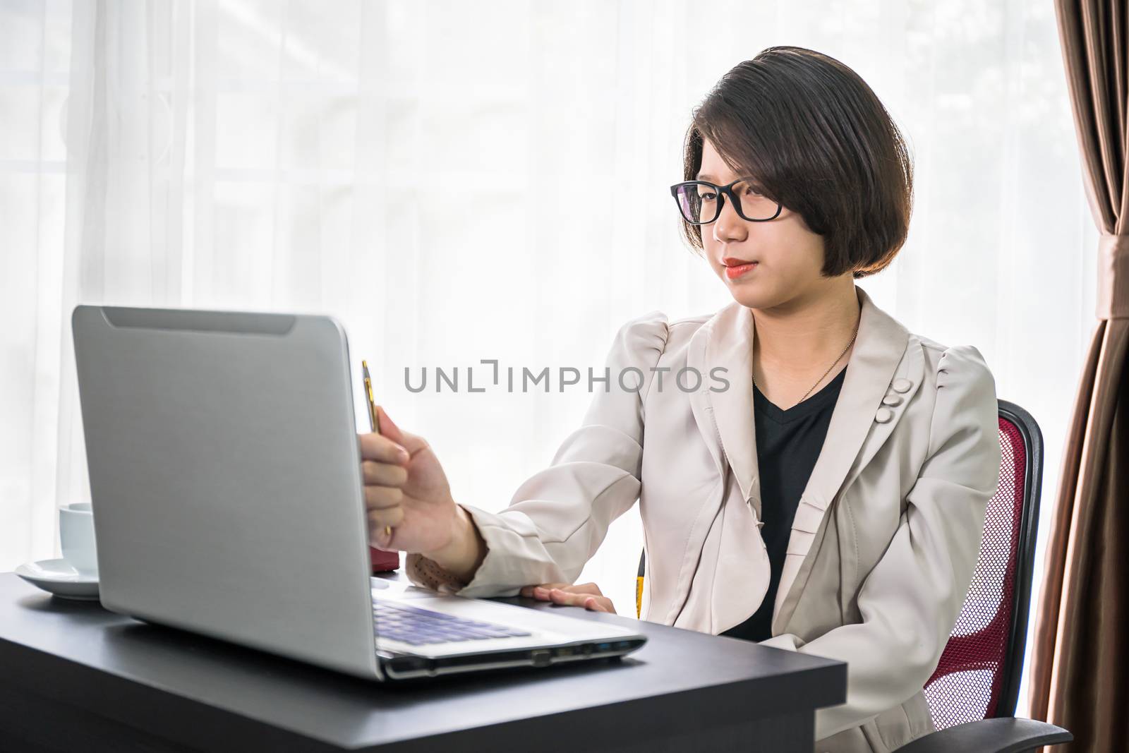 Young asian woman short hair in smart casual wear working on laptop while sitting near window in home office