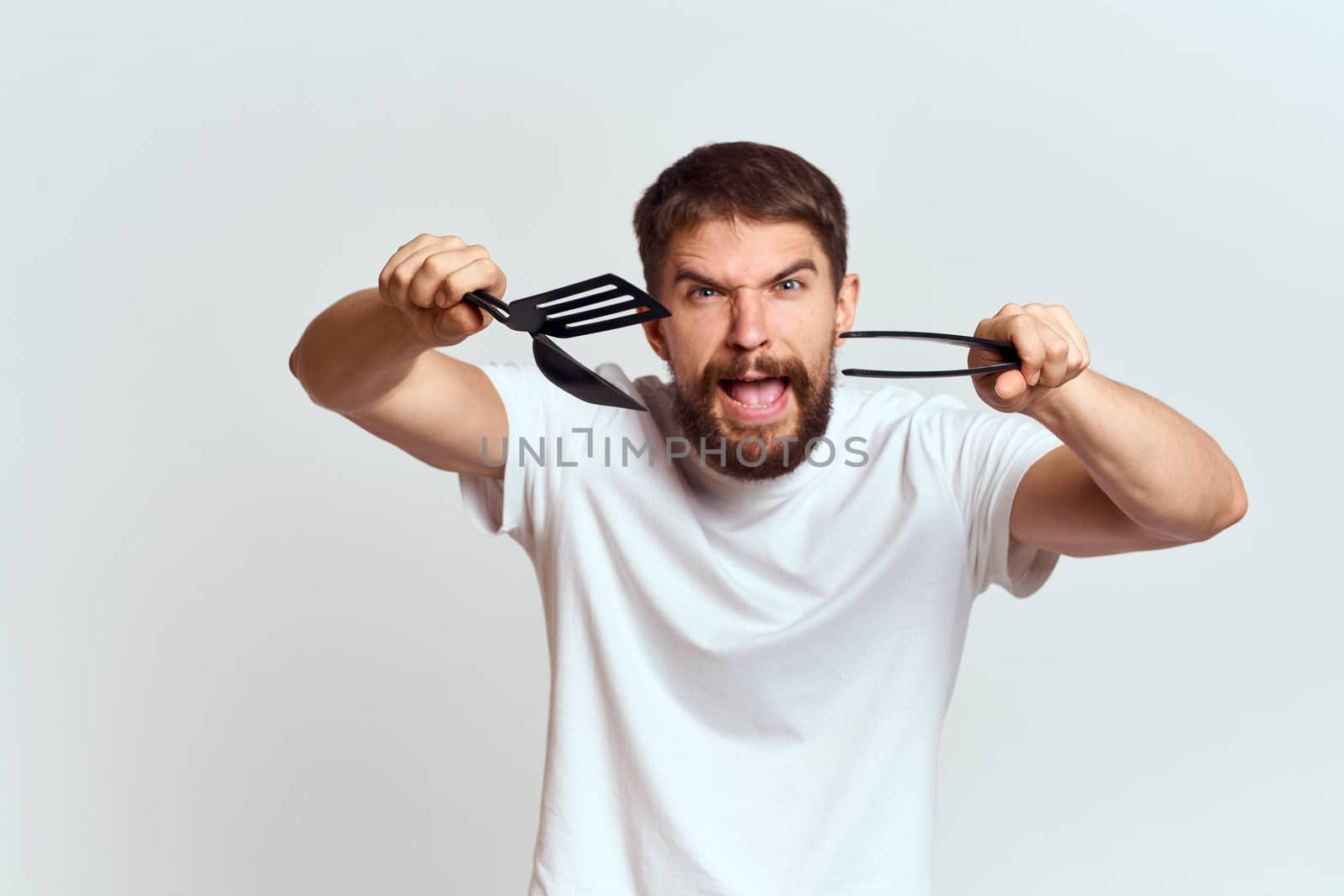A man with kitchen appliances in the hands of their white T-shirt on a light background cropped view by SHOTPRIME