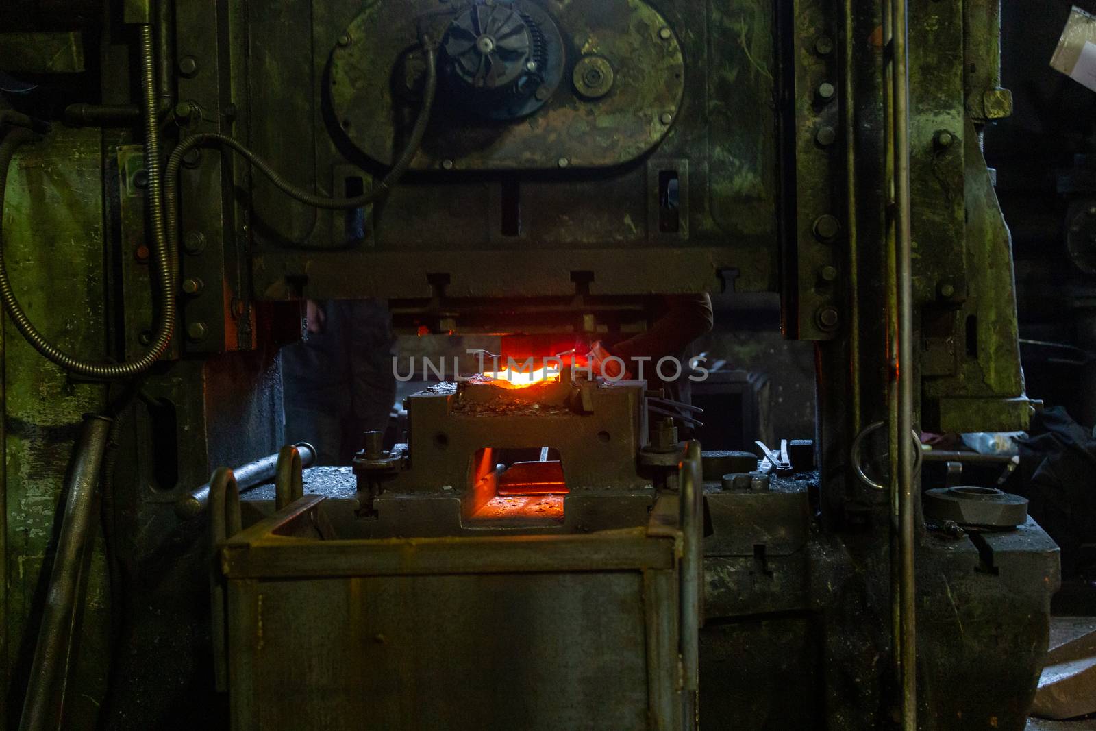 Close-up picture of fresh forged hot steel workpieces after press forming in dirty dark factory. Selective focus on foreground.
