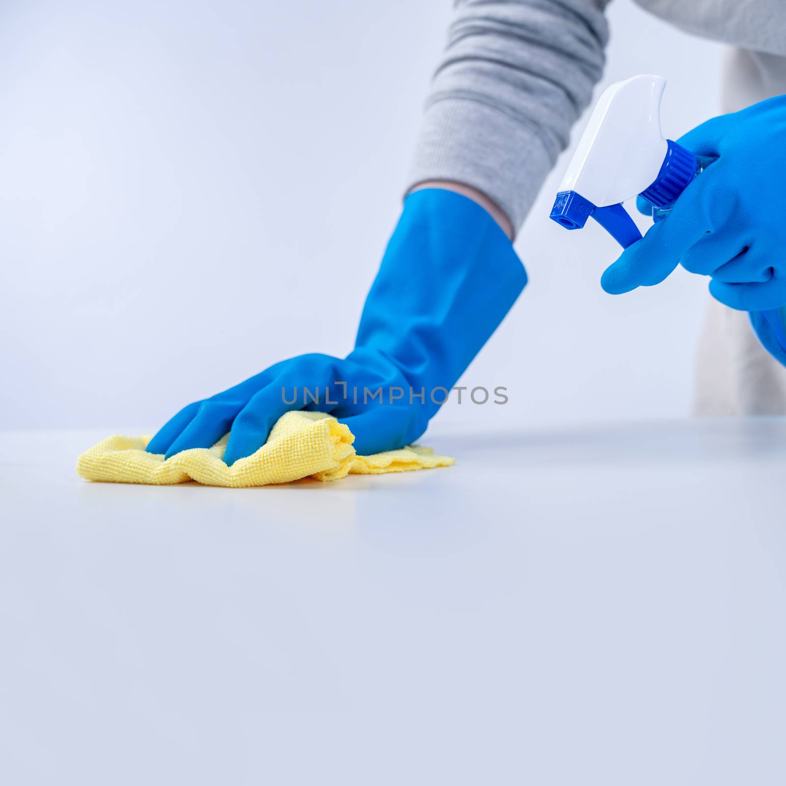 Young woman housekeeper in apron is cleaning, wiping down table  by ROMIXIMAGE