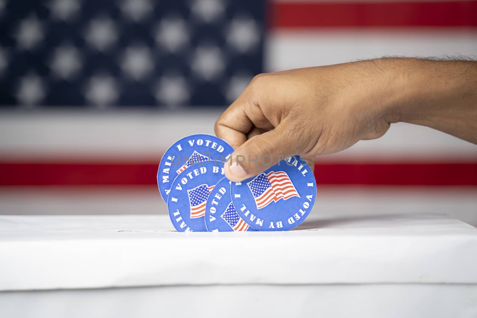 Close up of hands putting multiple I voted my Mail stickers inside the box with US flag as background - Concept of Vote by mail fraud in USA elections