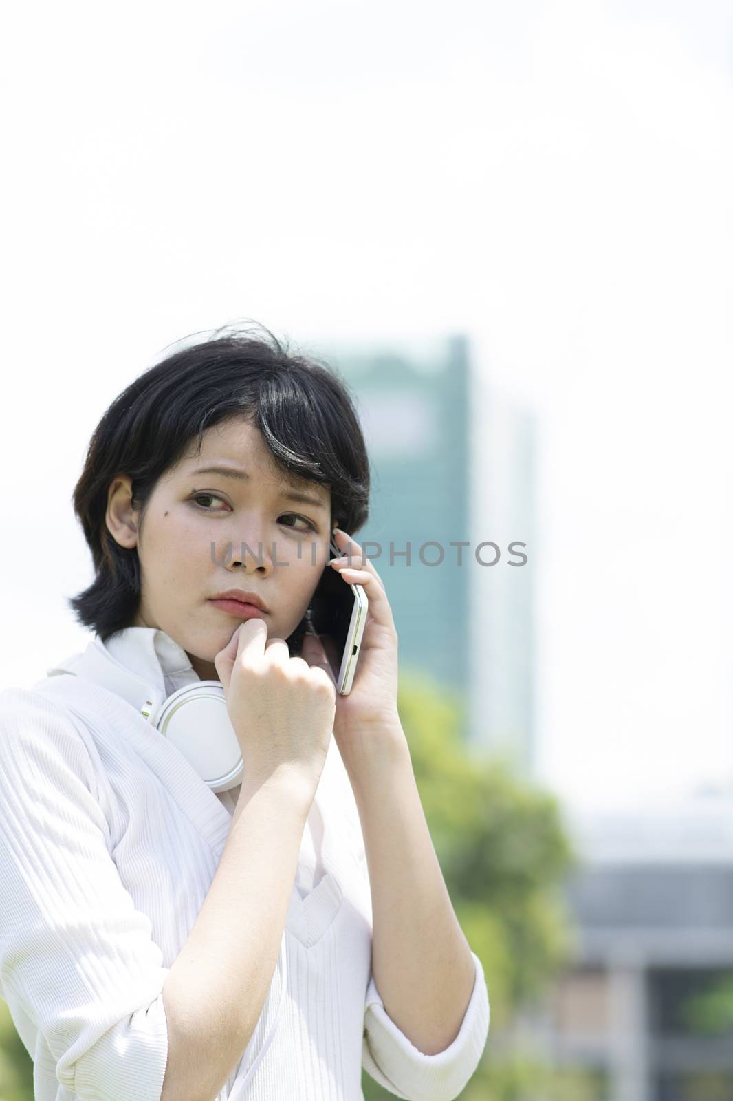 Worrying asian woman making phone call in garden. Blurry building background.