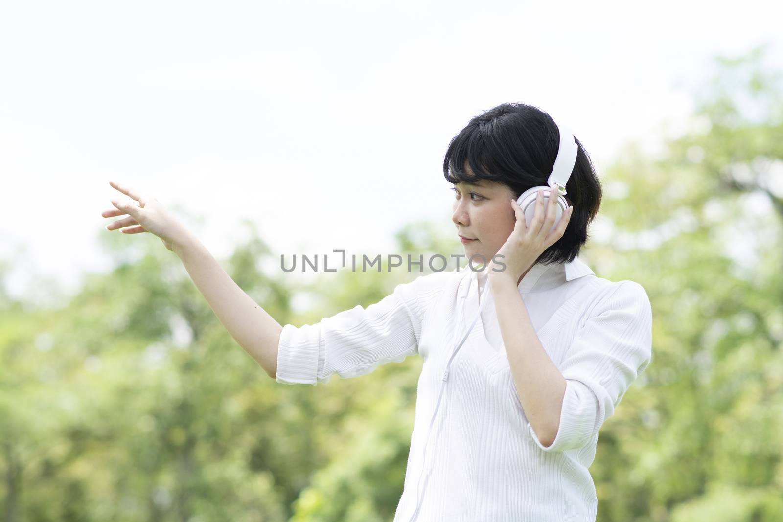 Happy asian woman listening to music on mobile phone in garden. 