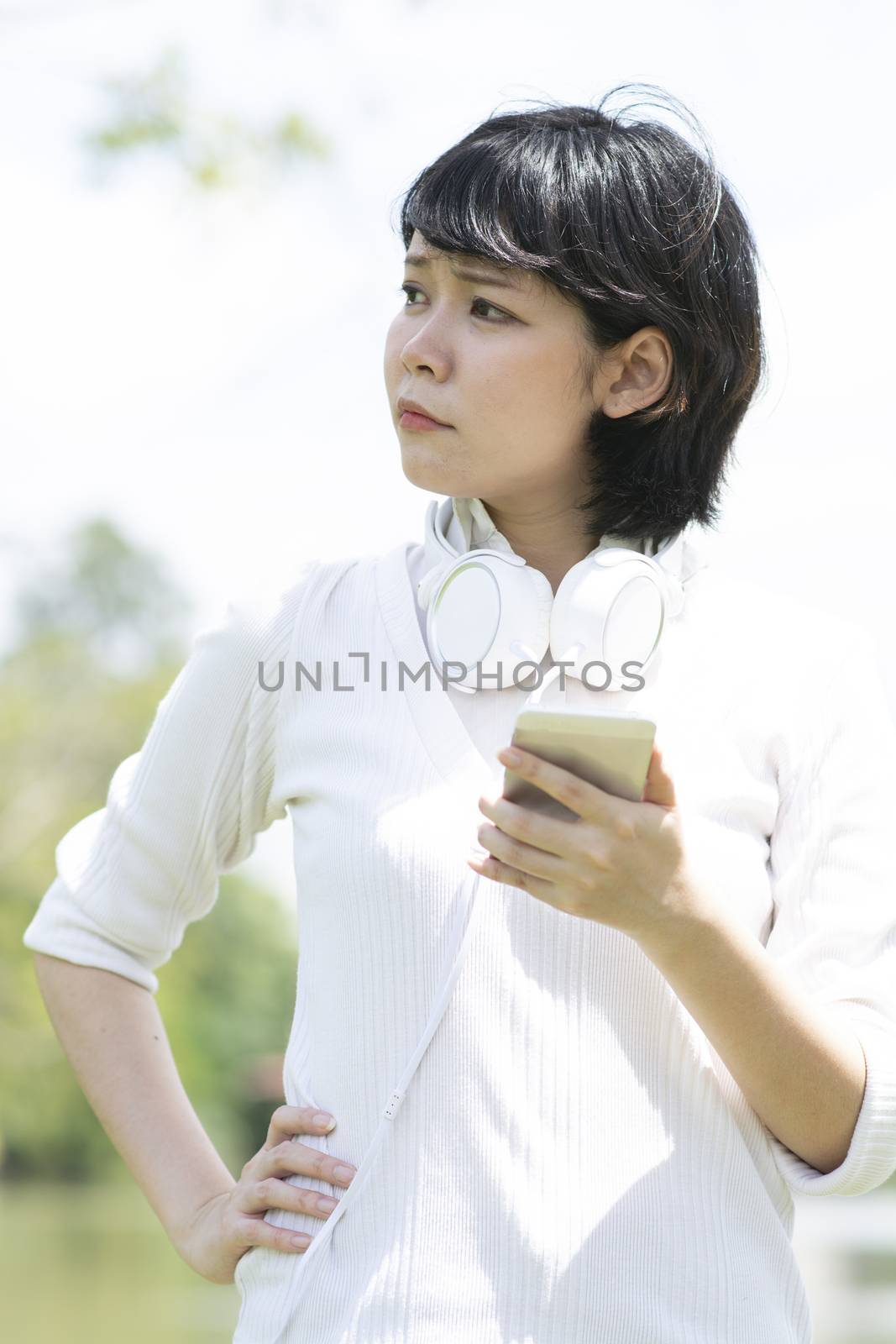 Worrying asian woman making phone call in garden. Blurry building background.