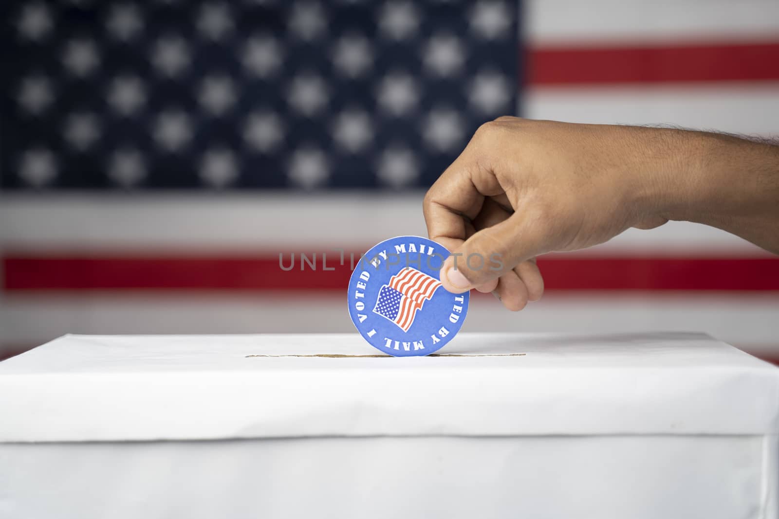 Close up of hands Dropping I voted my Mail stickers inside the ballot box with US flag as background - Concept of Vote by mail or Mail-in voting at USA elections