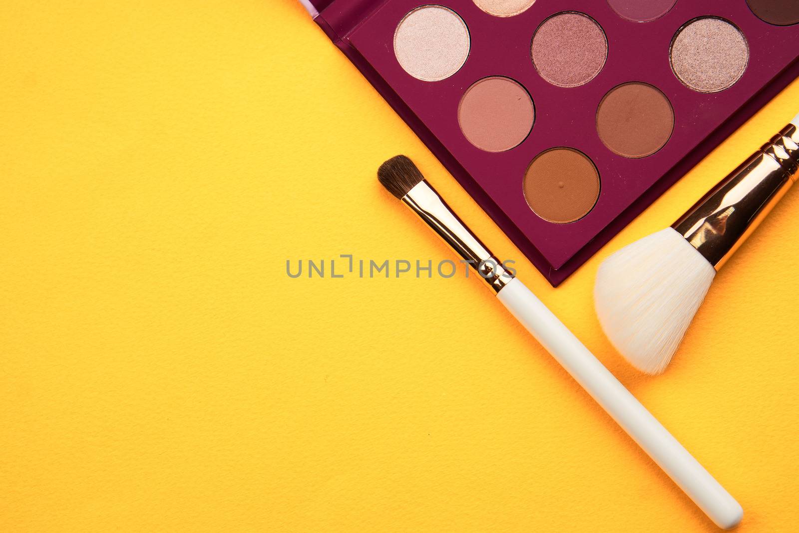 Eyeshadows and makeup brushes on a yellow background top view professional cosmetics by SHOTPRIME