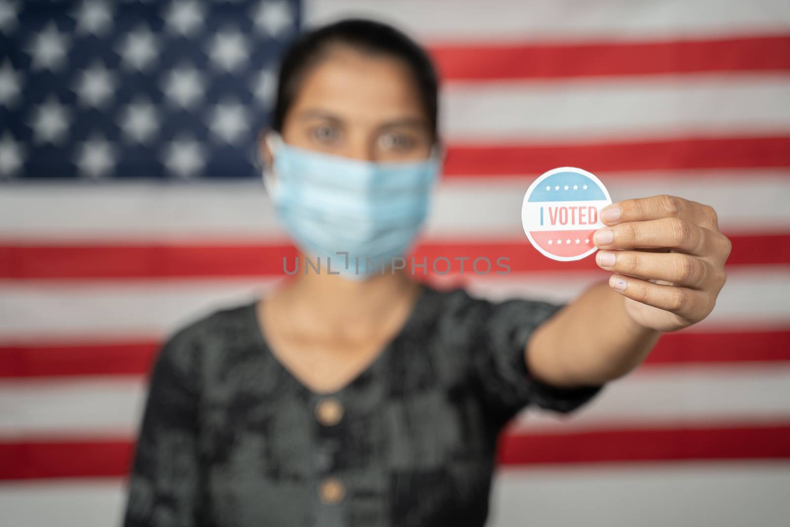 Girl with mask showing I voted Sticker with US flag as background - Concept of voting during US election