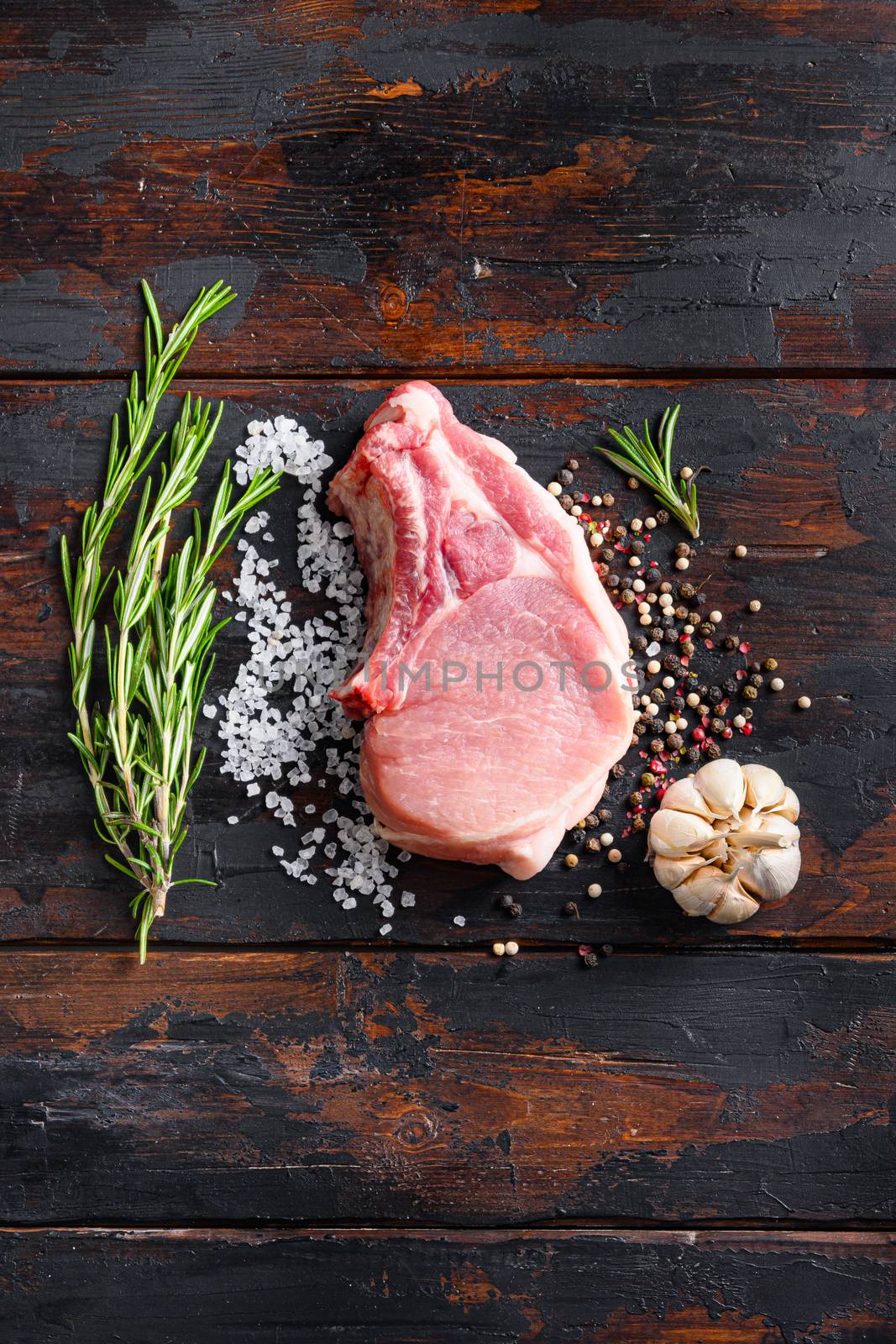 Raw meat on dark wood rustic background. Bio organic farm pork steak with herbs and spices. Cooking meat. Copy space. Top view vertical space for price or text.