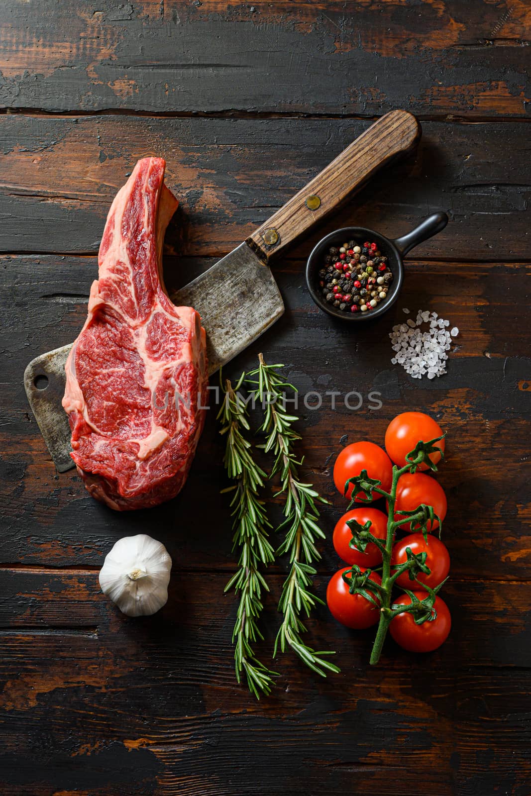 Fresh tomahawk steak on meat cleaver. Organic farm marbled prime black angus beef. Dark wooden background. Top view. With seasonings, peppercorns, chilie, rosemary,salt,garlic. by Ilianesolenyi