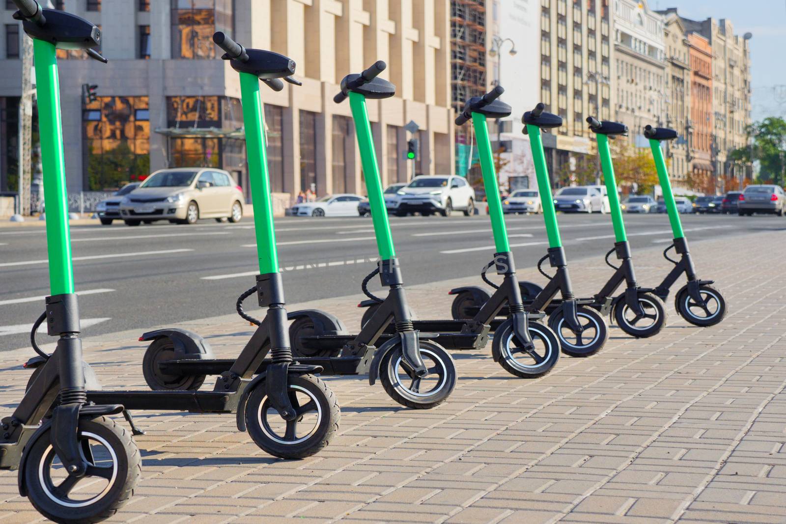 Eco transportation concept. Scooter rental in the city. Environment conservation. Eco friendly transportation. Vehicle rent service concept. Electric scooters in line on urban city background by synel