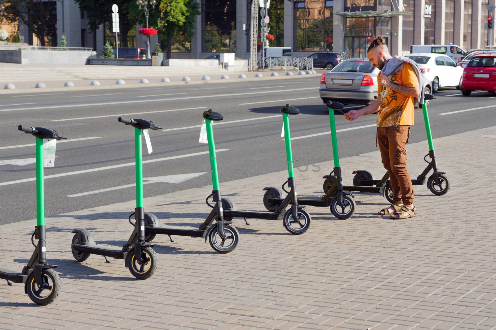 Tourist man take electric kick scooter in sharing parking lot. New sharing business project started in city, eco transportation. Scooter rental background. Electric scooters for rental by synel