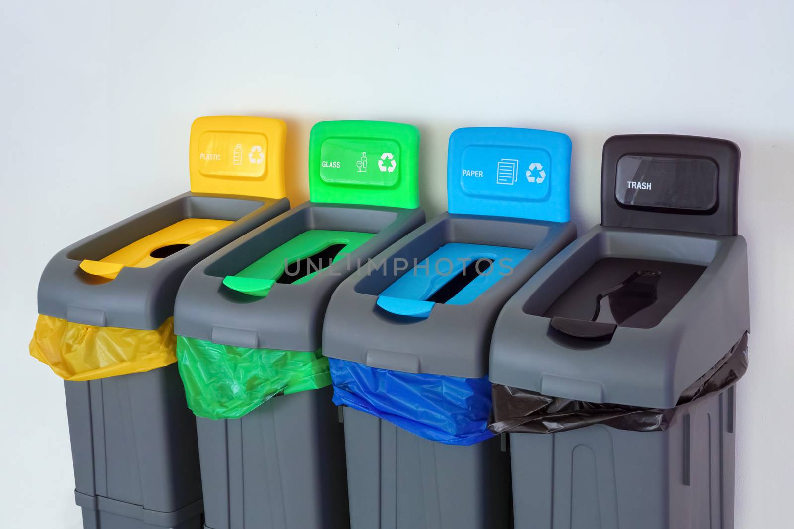 Four plastic waste bins outside. Different colored bins for collection of recycled materials. Garbage bins with garbage bags of different colors. Environment, ecology, conceptual. Saving planet idea