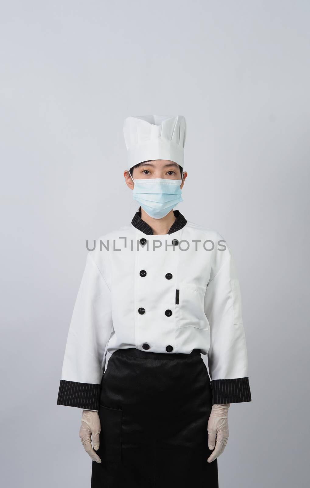 Asian woman chef in white color uniform with hygienic such as medical face mask and rubber hand glove for prevent or protect covid-19 or coronavirus pandemic. Studio shot and copy space.