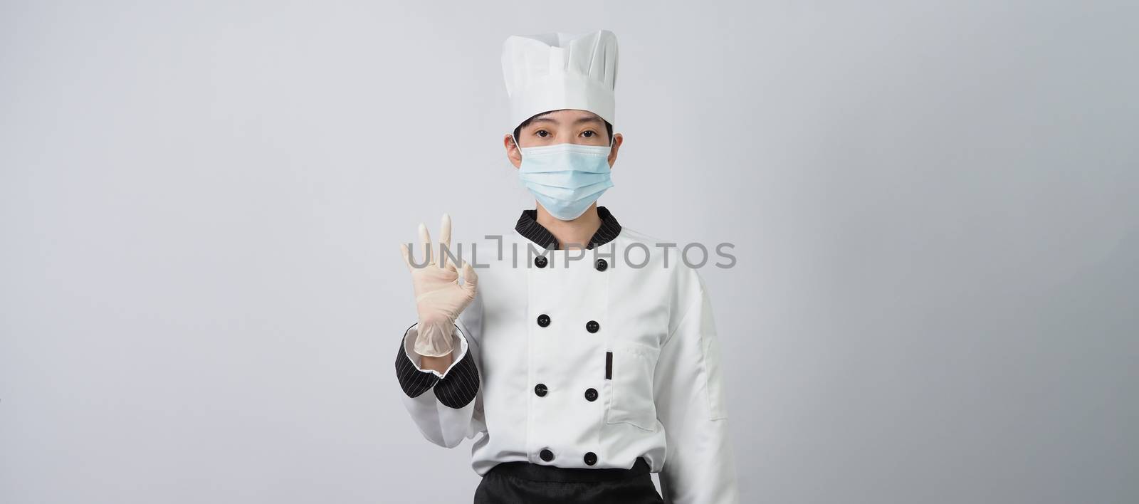 Asian woman chef in white color uniform with hygienic such as medical face mask and rubber hand glove for prevent or protect covid-19 or coronavirus pandemic. Studio shot and copy space.