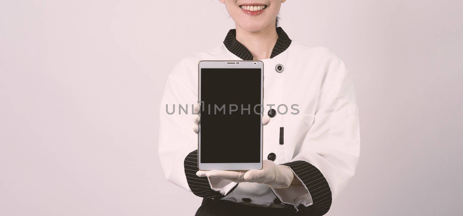 Middle aged of asian woman chef holding smartphone or digital tablet and received order from online shop or merchant application. she smiling in chef uniform and standing in studio with white color background.