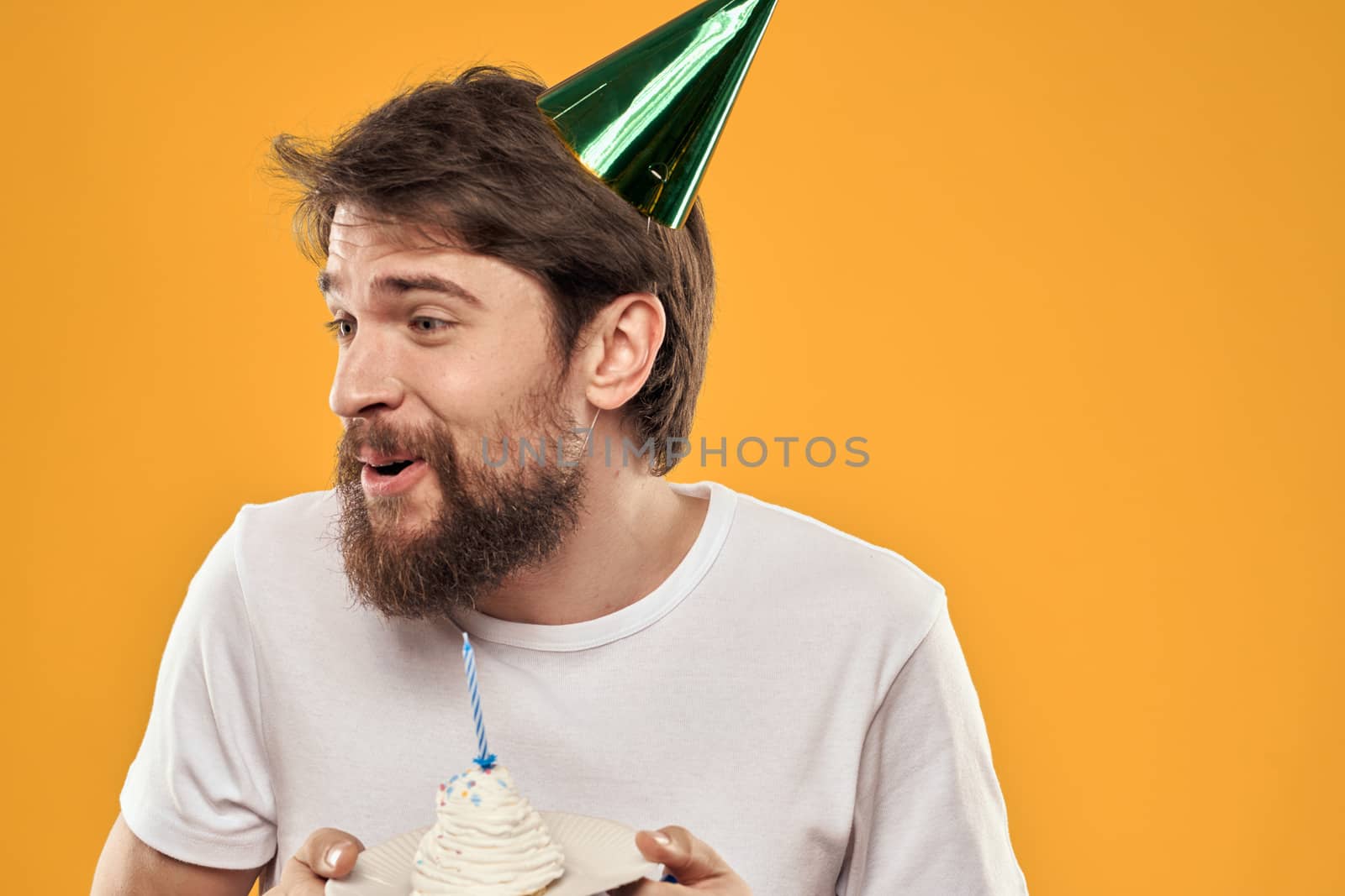 Handsome man with a beard and in a cap celebrating a birthday party yellow background. High quality photo