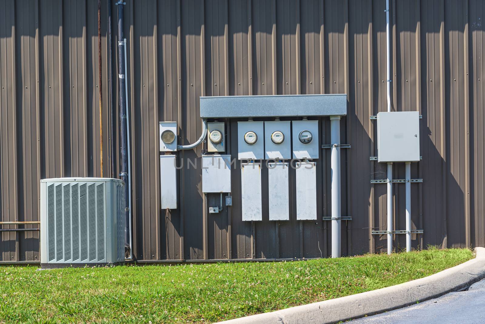 Horizontal shot of an air conditioner and electric meters outside of an office complex.
