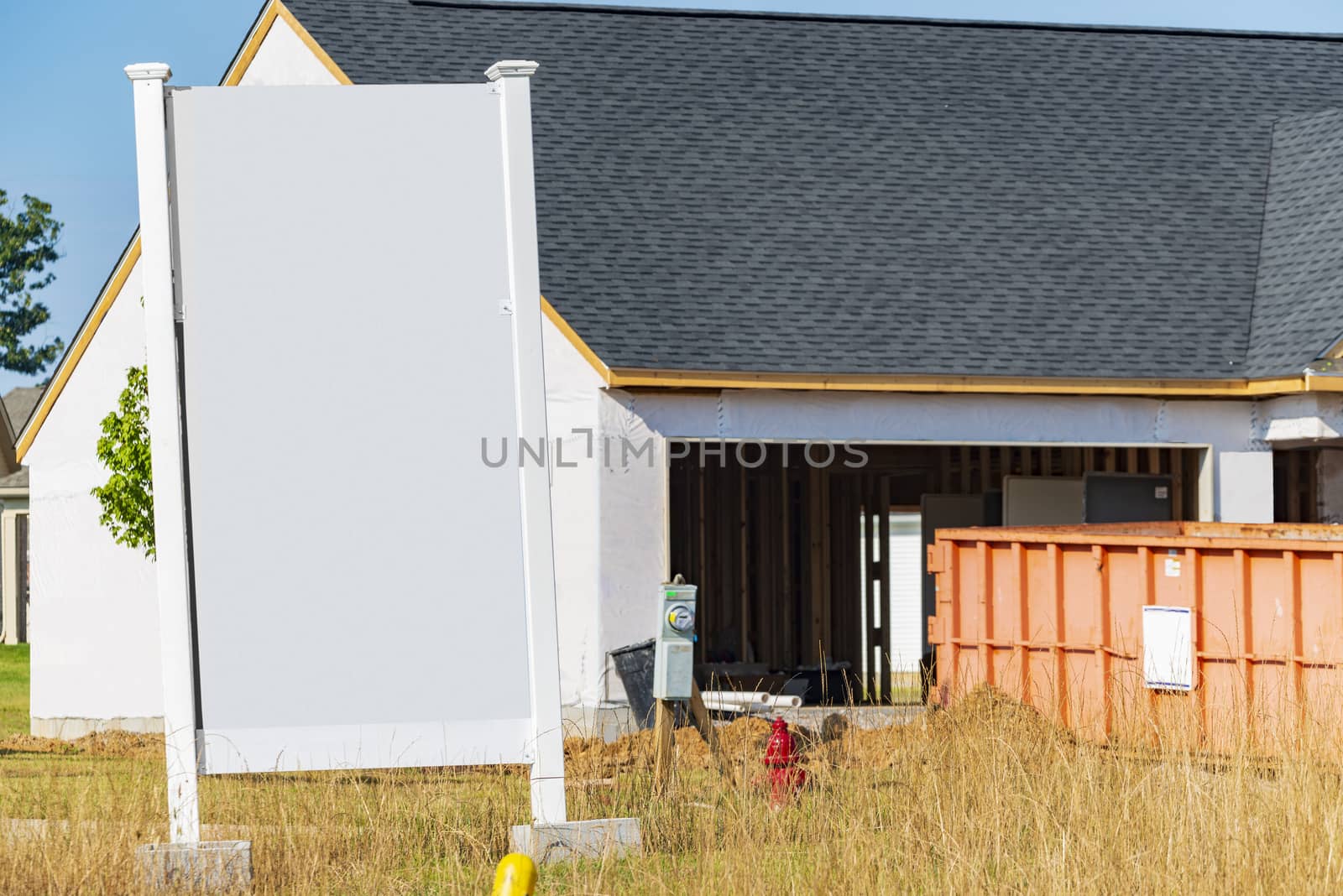 Horizontal shot of a big blank white sign in front of a new home that is under construction.