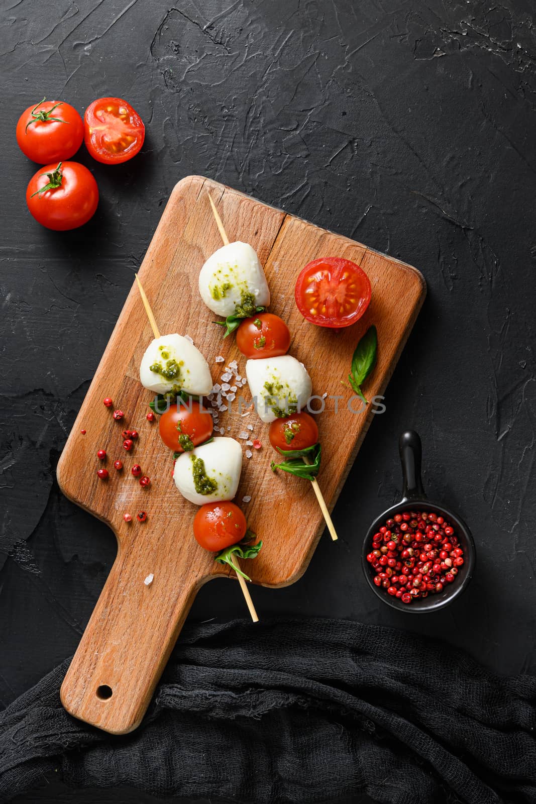 caprese salad skewer with tomato on sticks Italian traditional caprese salad ingredients. Mediterranean food. over black stone background overhead space for text vertical by Ilianesolenyi