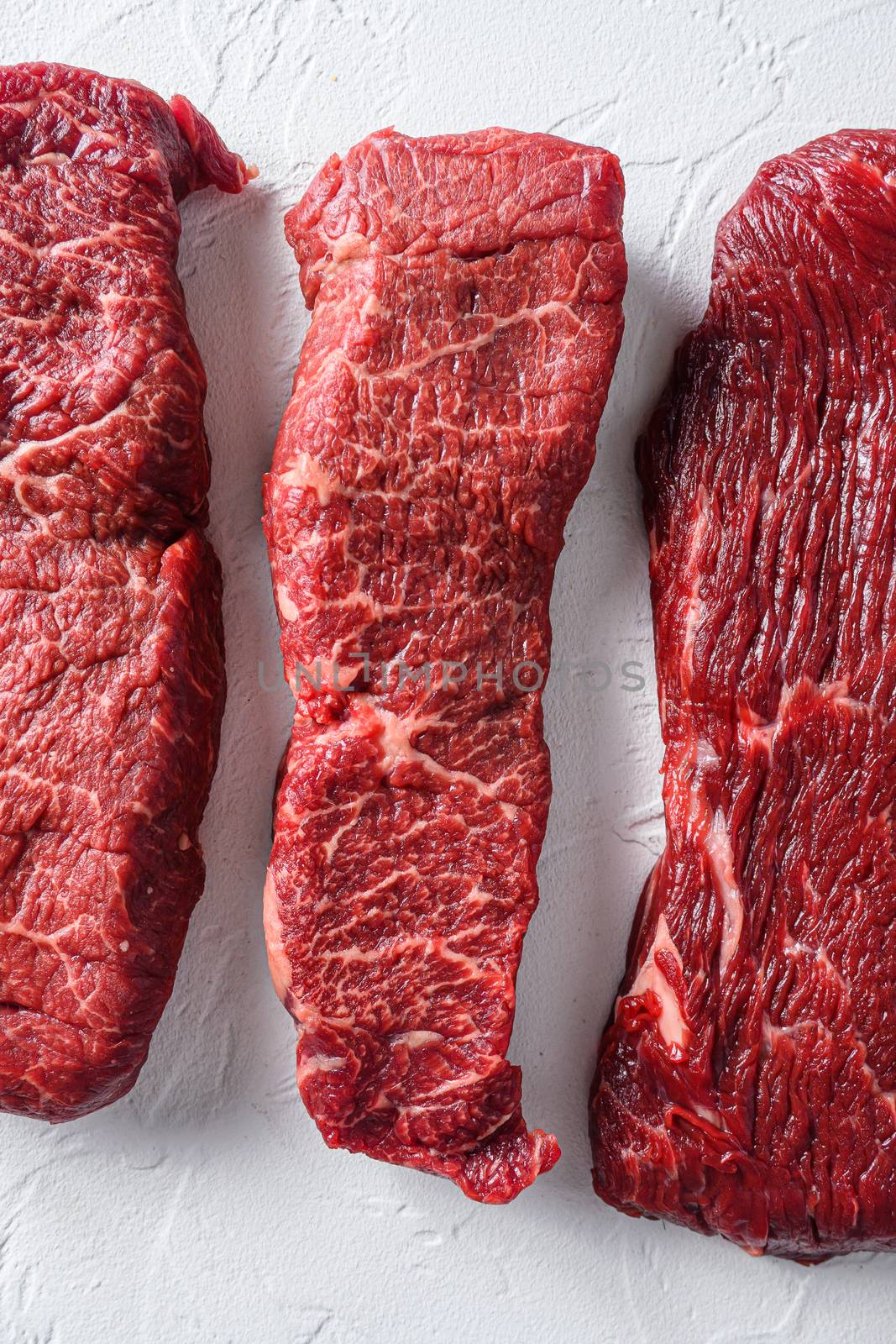 Raw whole denver steak for BBQ cut organic meat cut top view close up over white concrete background vertical