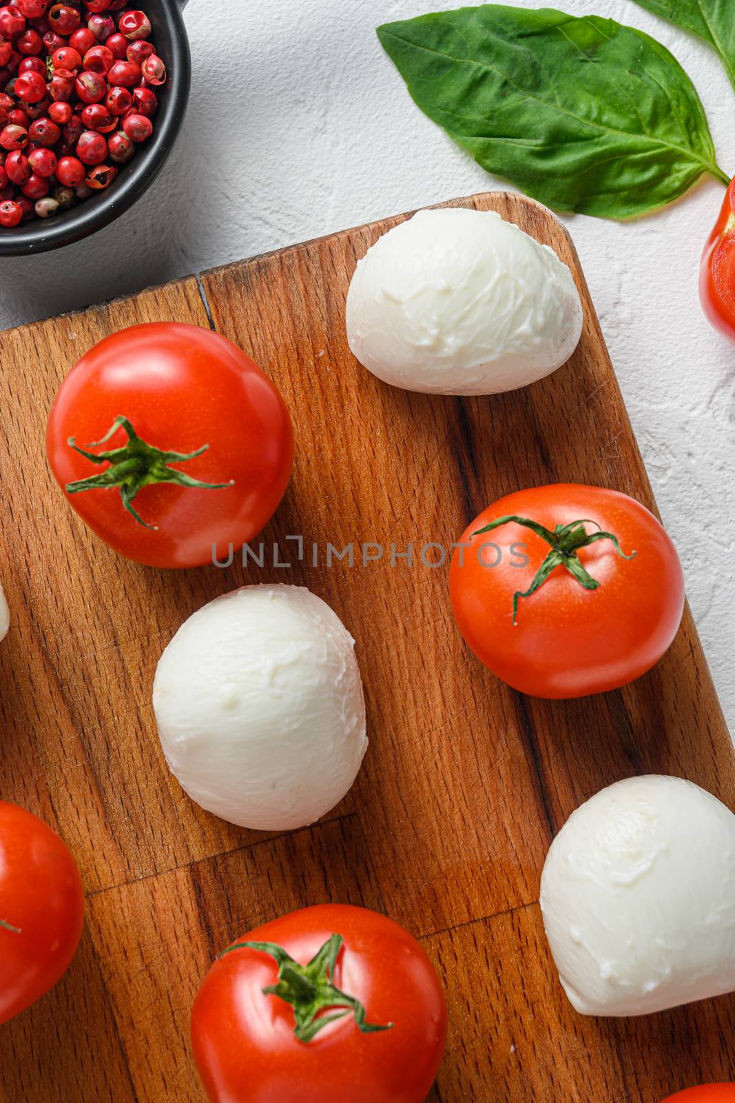 Mini balls of mozzarella cheese, on chop wood board ingredients for salad Caprese. over white background. close up selective focus vertical.