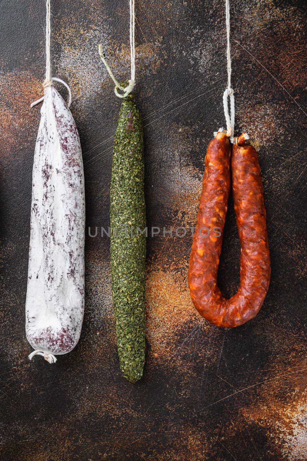 Dry cured chorizo and fuet salami sausages hanging on dark background.