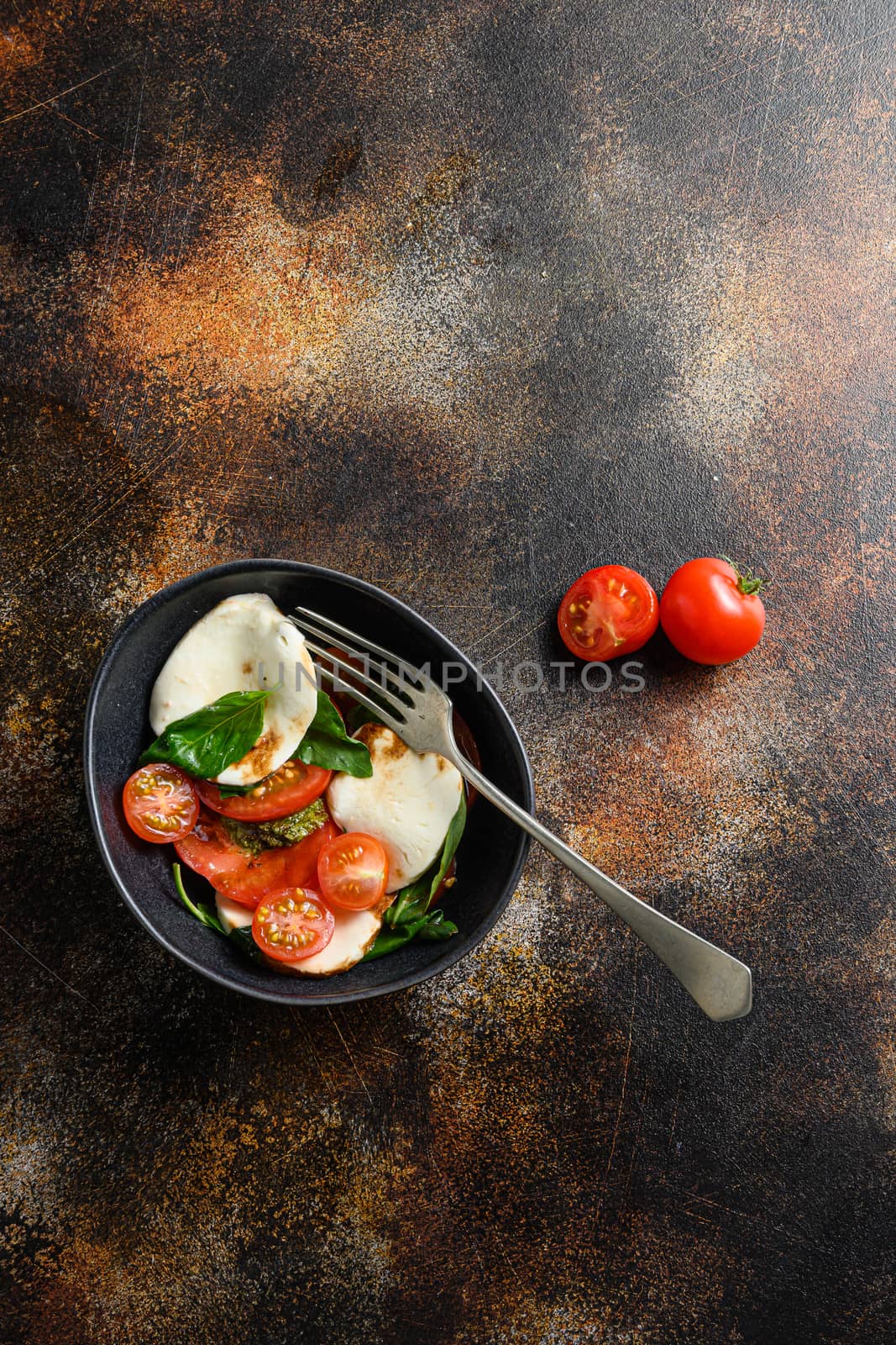 Tomato, basil, mozzarella Caprese salad ib bowl with fork with balsamic vinegar and olive oil. old rustic background over head top view space for text vertical by Ilianesolenyi