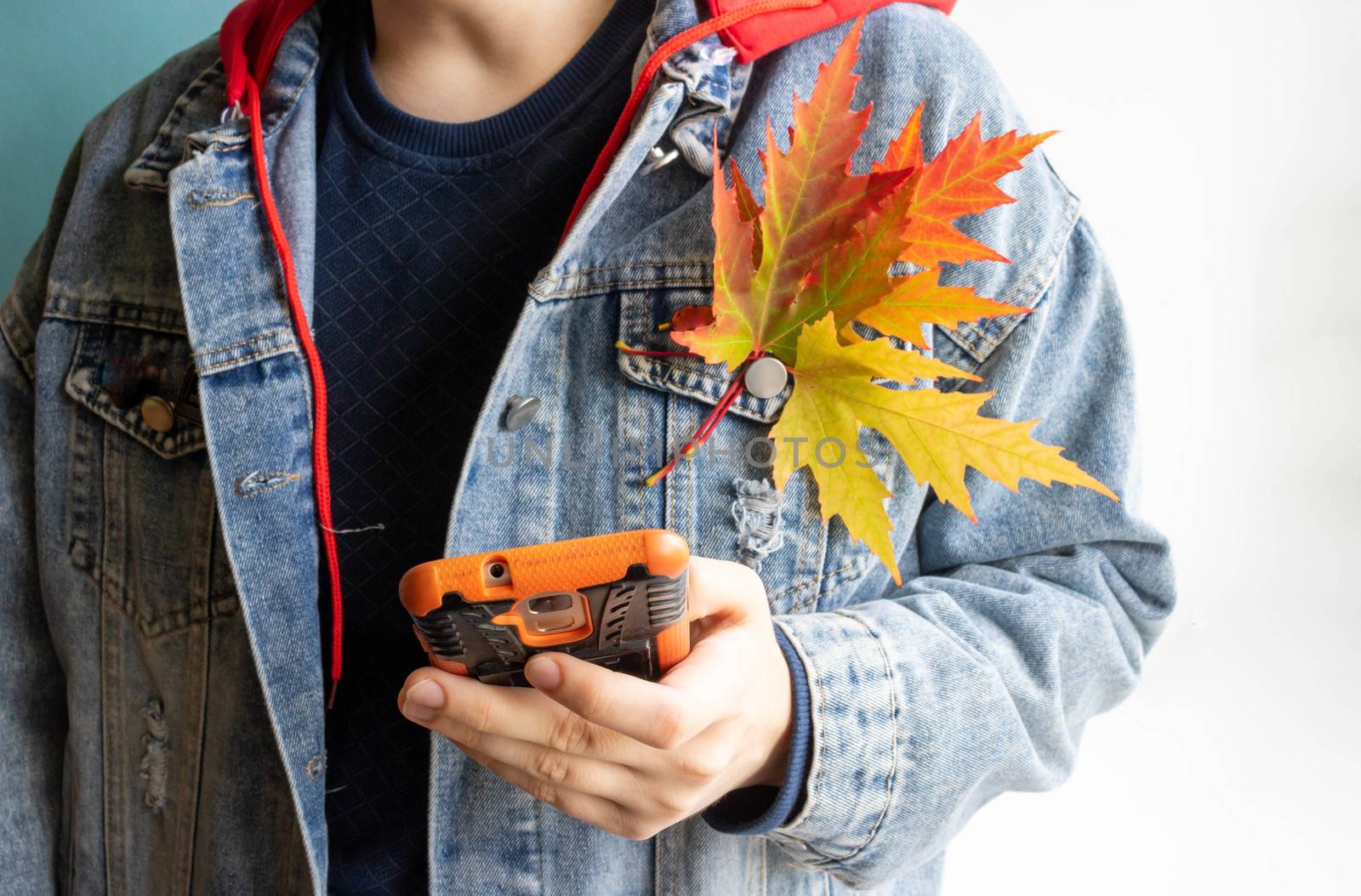 A teenager in a denim jacket with maple leaves holds a phone in his hand.