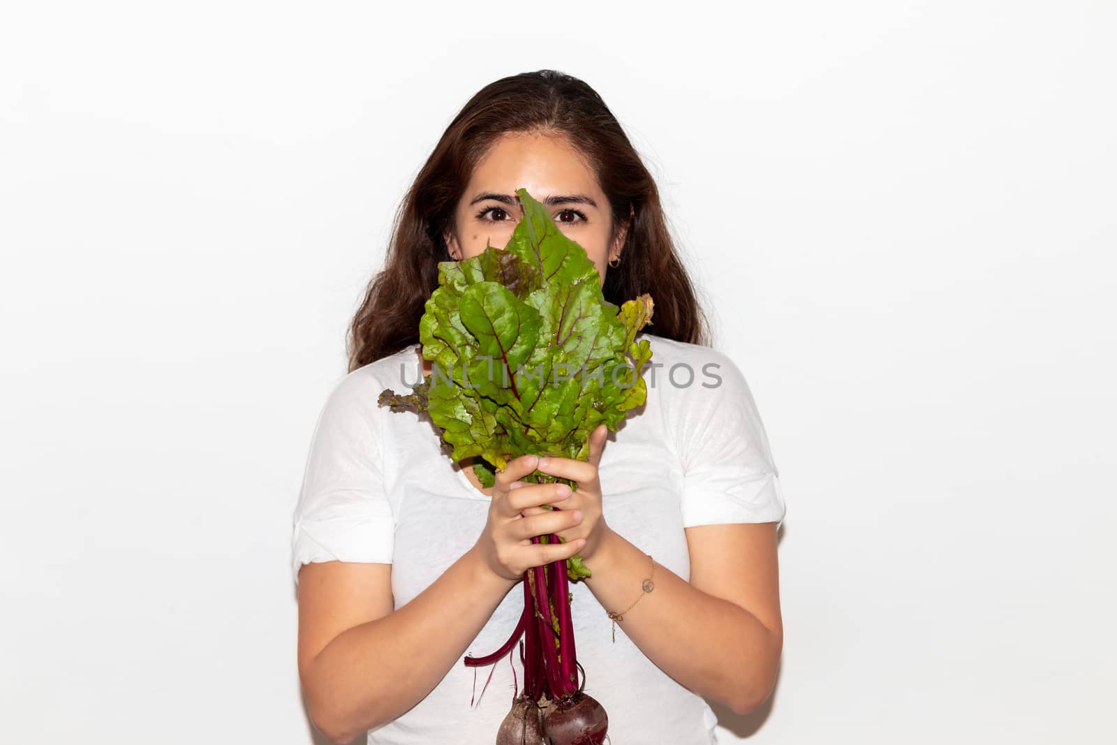 Real young man with a bunch of radishes covering his face. Isolated on a white background. by leo_de_la_garza