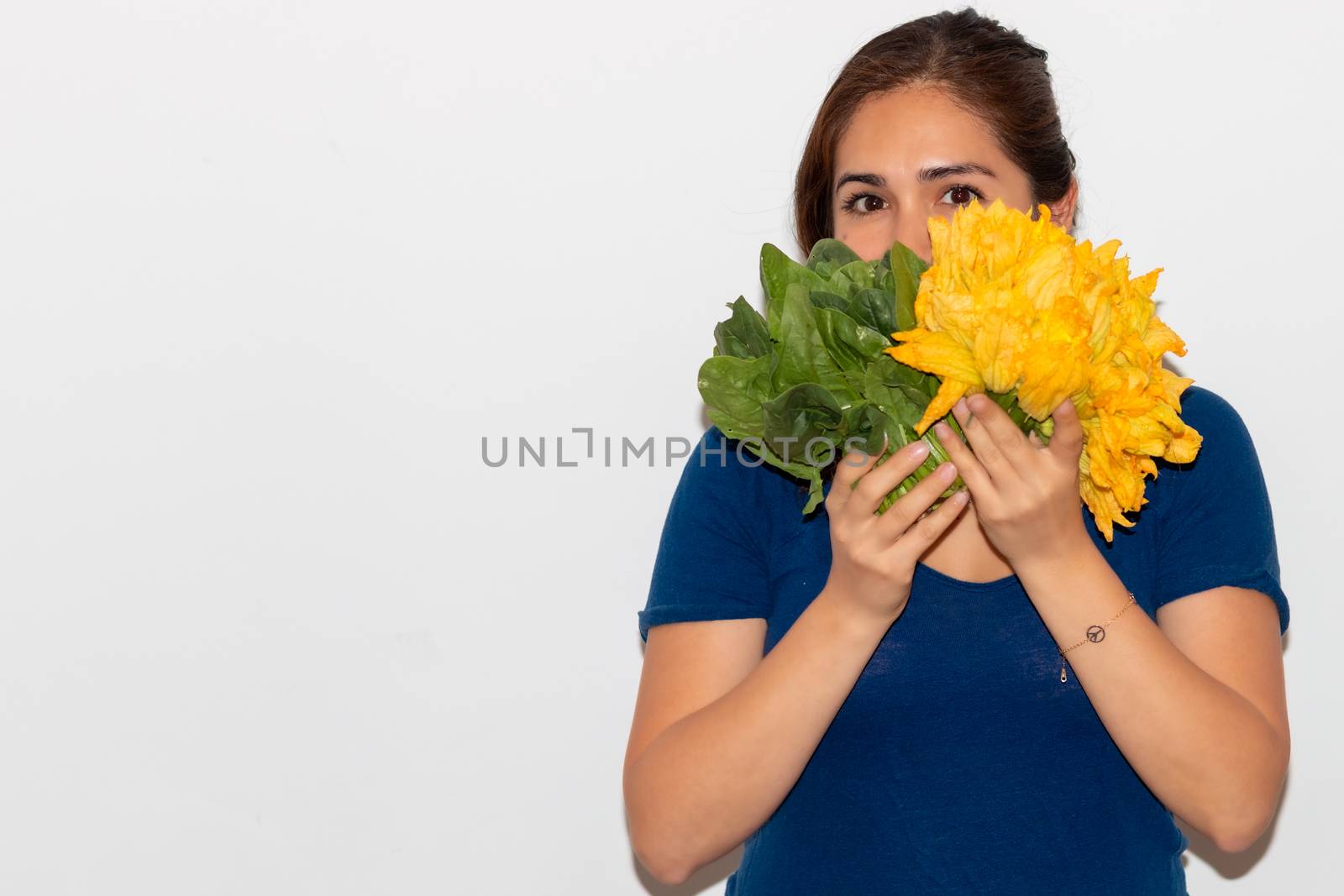 Real young man with a bunch of pumpkin blossom and spinach covering his face. Isolated on a white background. by leo_de_la_garza