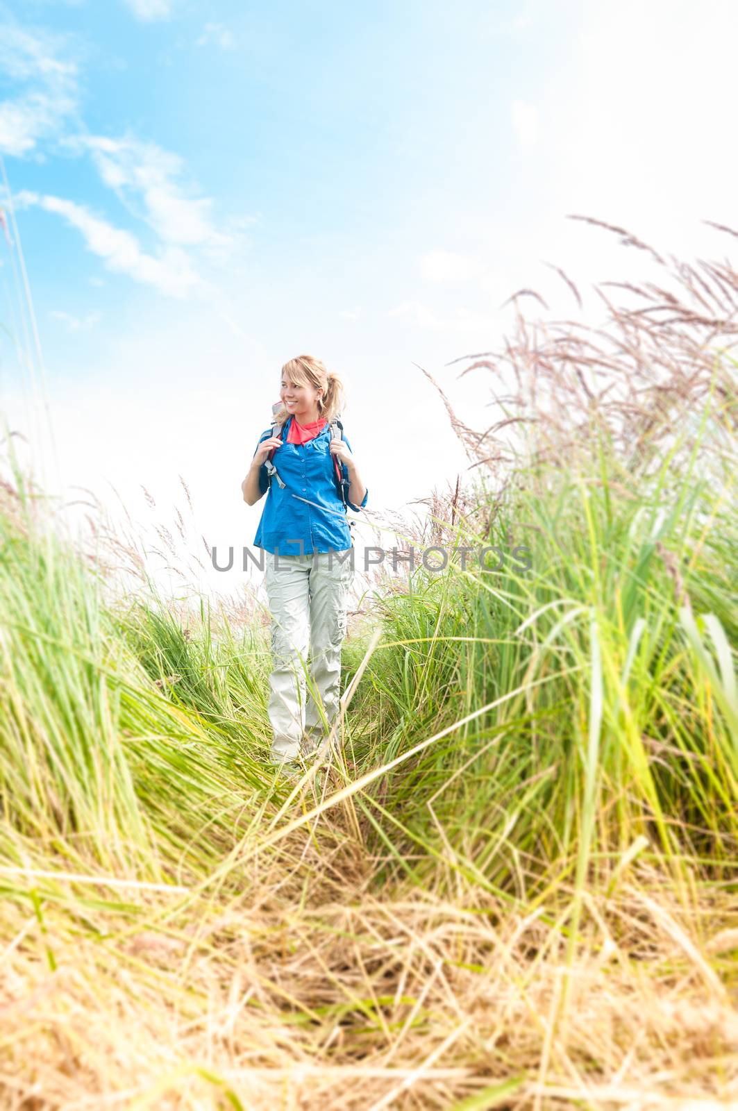 Young girl walking in meadow with backpack on. by Yolshin