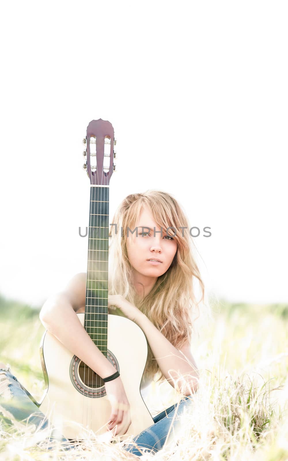 Pretty girl with guitar sitting on ground. Beautiful woman with blonde hair holding musical instrument and smiling. Green grass as background. Sunny summer day. Outdoor activity for young people.