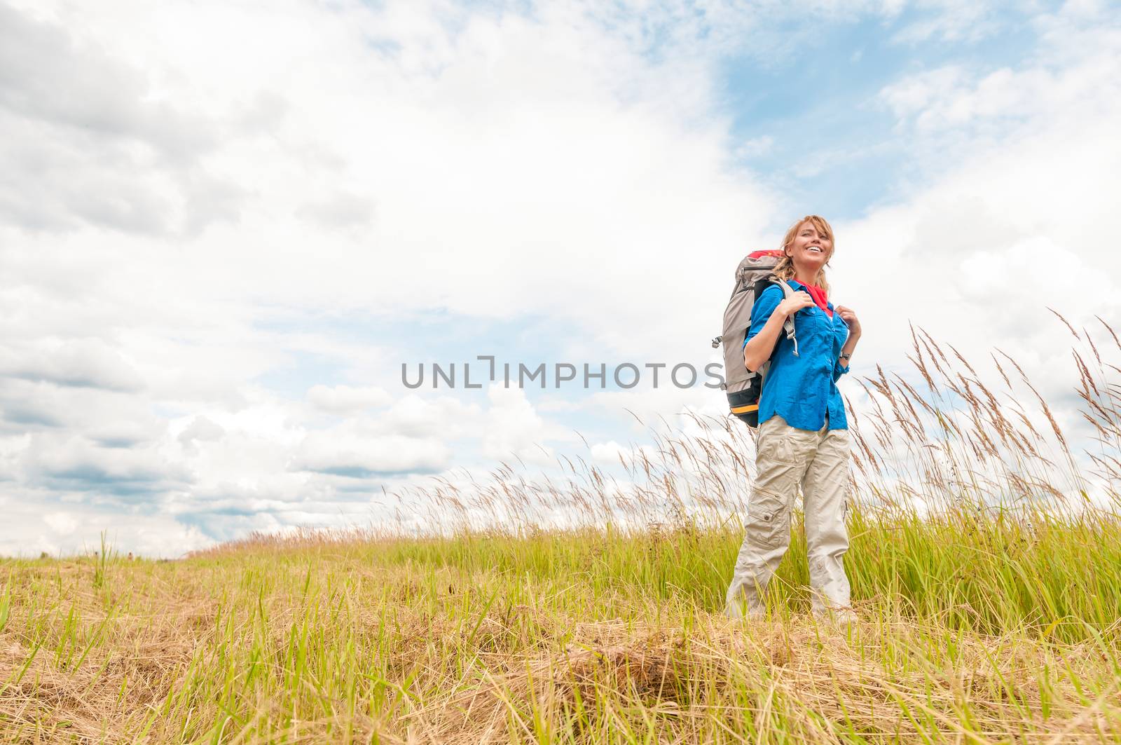 Young girl walking in meadow with backpack on. by Yolshin
