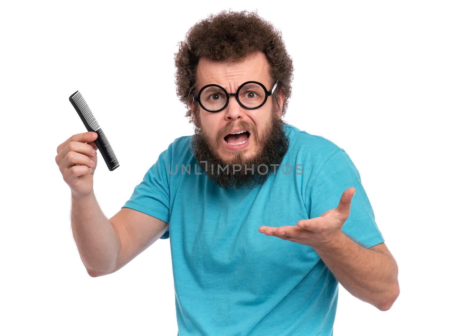 Crazy bearded Man with funny Curly Hair tries to comb his tangled and naughty hair with a small black hairbrush. Surprised face of guy in eye Glasses who holds comb, isolated on white background.