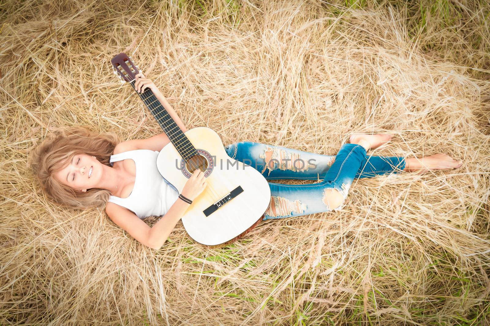 Beautiful woman dreaming with closed eyes. Pretty girl lying in meadow with guitar. Person holding musical instrument. Happy smiling girl with carefree lifestyle. Outdoor activity for young people.