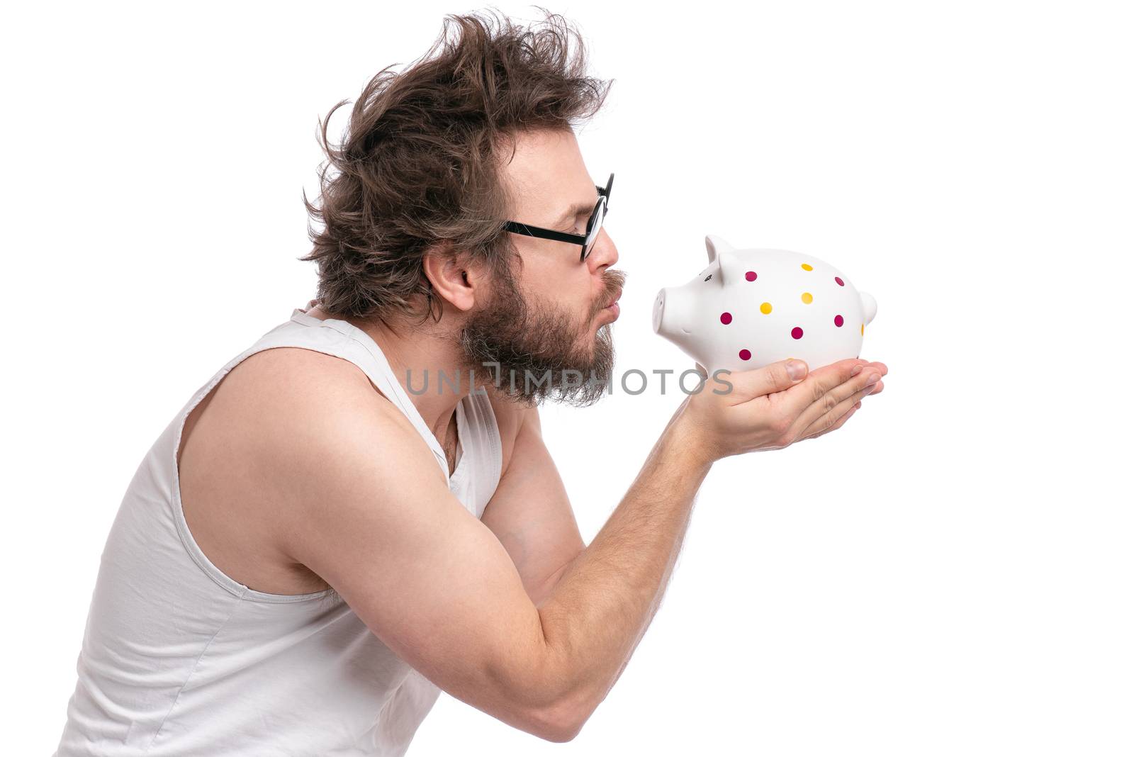 Crazy bearded Man with funny Haircut in eye Glasses holding Piggy Bank, isolated on white background. Saving Money concept. Male carefully kisses his piggybank.