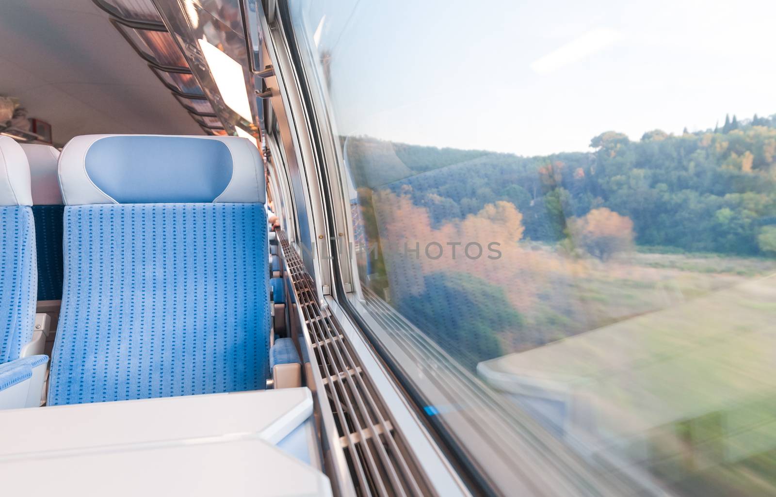 Inside cabin of modern express train. Nobody in blue chairs at window. Motion blur. Comfortable chairs and table in foreground, nature outside window. Travel, France, Europe.