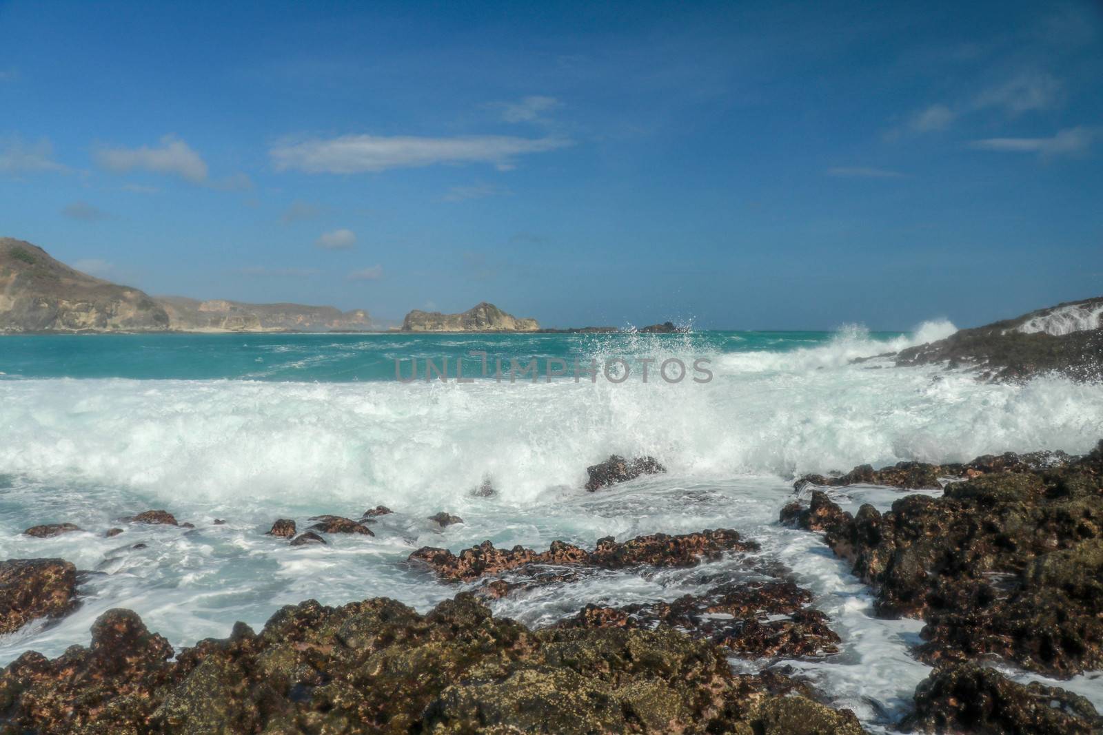 Waves splashing on sharp cliffs of Tanjung Aan beach. Dangerous phenomenon on a heavenly beach. Water is bubbled from the strength of the crushing waves. Beauty of the nature.