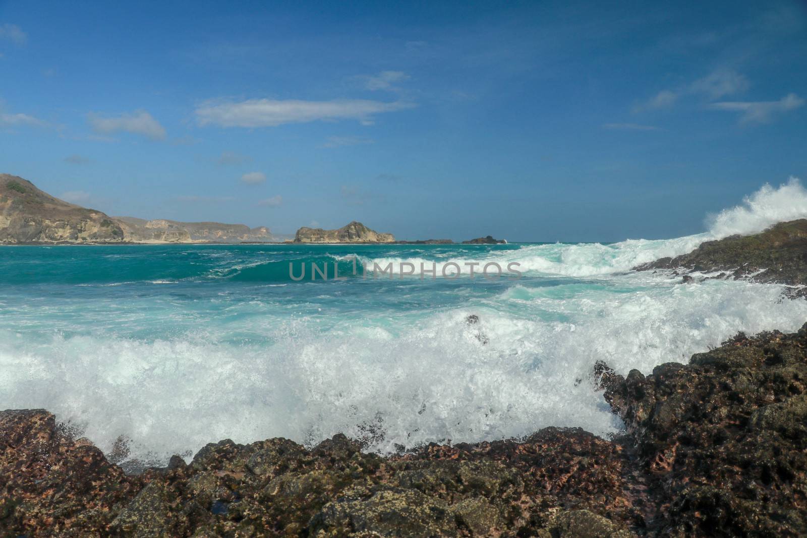 Waves splashing on sharp cliffs of Tanjung Aan beach. Dangerous phenomenon on a heavenly beach. Water is bubbled from the strength of the crushing waves. Beauty of the nature.