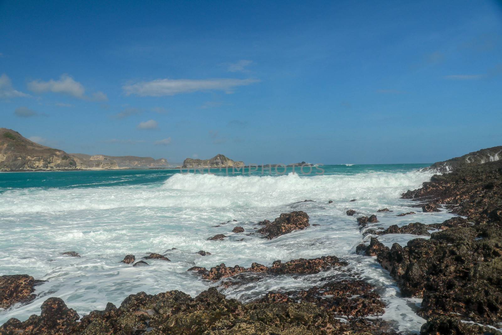 Waves splashing on sharp cliffs of Tanjung Aan beach. Dangerous phenomenon on a heavenly beach. Water is bubbled from the strength of the crushing waves. Beauty of the nature.