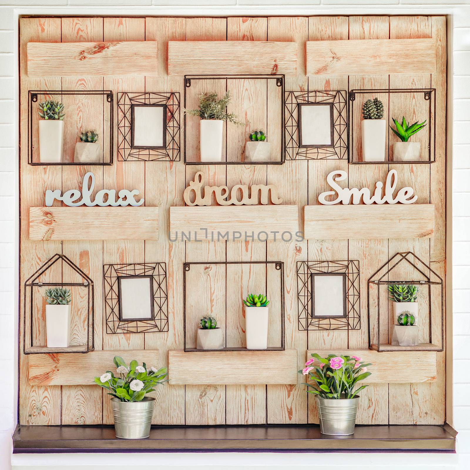 Decorative hanging on the wall. Rustic style in interior, exterior decoration. Wooden wall decorated with white pots with green plants and photo frames. Vintage style, accessories, modern garden decor by synel