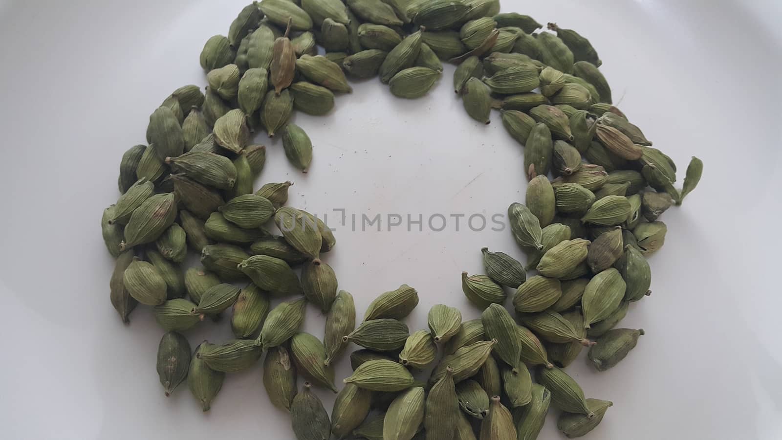 Closeup top view of dried green Elettaria cardamomum fruits with seeds, cardamom spice arranged in ring on a white background