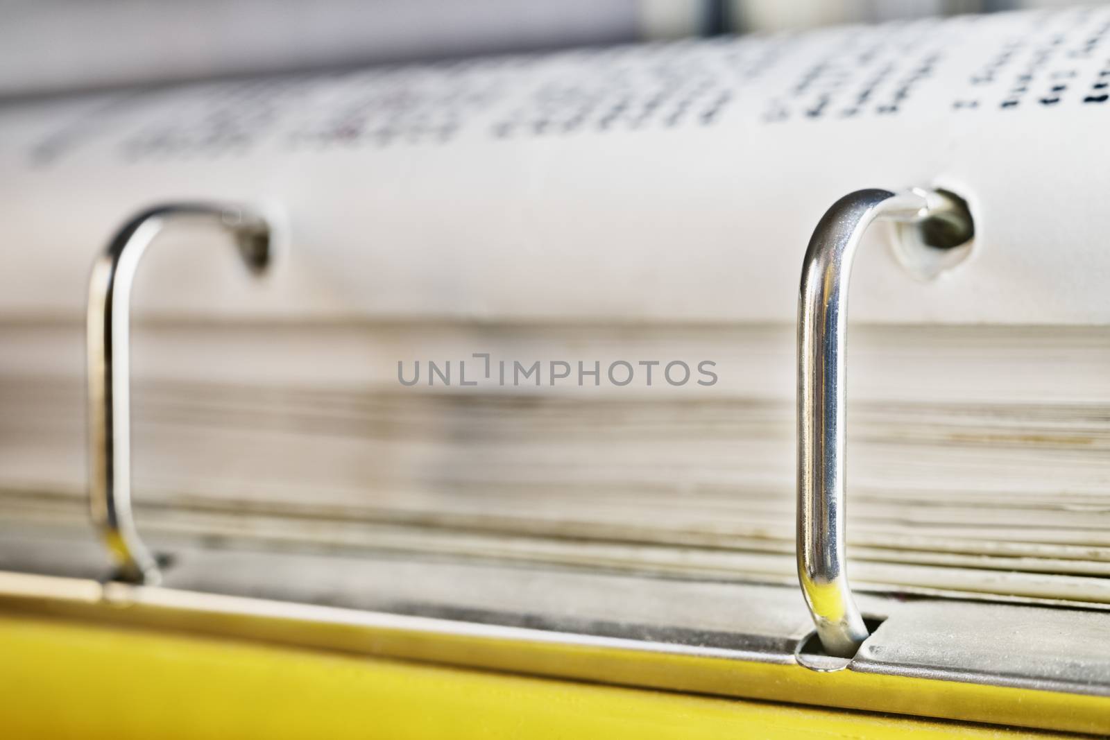 Open yellow binder close up , stack of white papers and bright metal rings , in the background black text out of focus