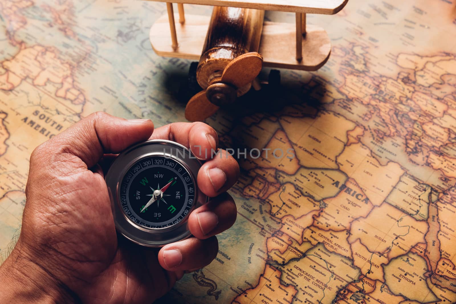 Hand hold old compass discovery and wooden plane on vintage paper antique world map background, Retro style cartography travel geography navigation