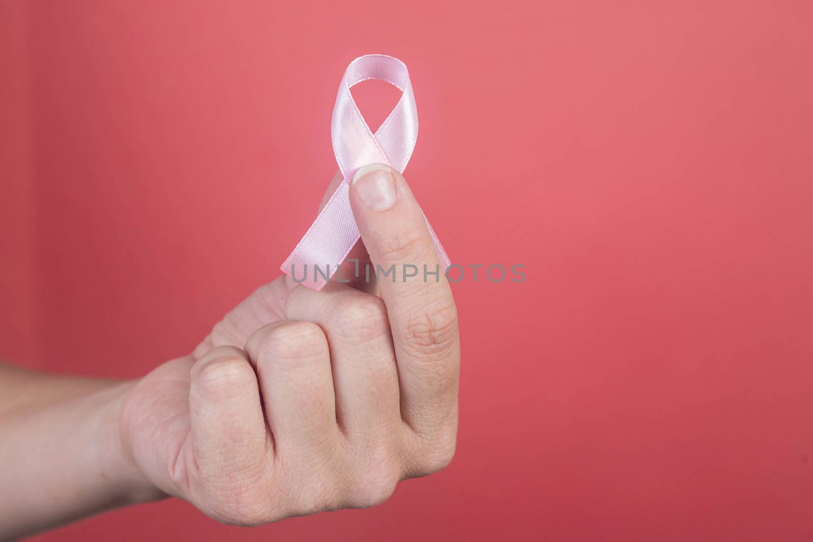 Pink ribbon on a woman hands on pink background. Breast cancer, healthcare and medicine concept, symbolic tape
